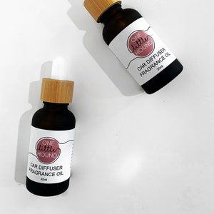 May include: Two brown glass bottles with bamboo caps and white labels. The labels have a pink circle with the text "ONE little HOUND" and the words "CAR DIFFUSER FRAGRANCE OIL 30ml".