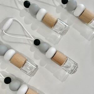 May include: Five car air fresheners with a string for hanging. Each air freshener has a clear glass bottle with a wooden cap and a silicone bead necklace with black, white and grey beads.