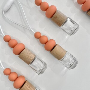 May include: Five car air fresheners with a string to hang them from the rearview mirror. Each air freshener has a wooden cap and a clear glass bottle. The wooden caps are attached to a string of orange silicone beads.
