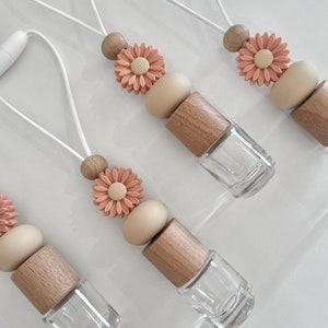 May include: Three car air fresheners with a wooden bead, a beige bead, and a peach-coloured flower charm. The air fresheners are hanging from white strings.