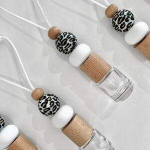 May include: Four white string car air fresheners with a wooden bead, a white bead, and a leopard print bead. Each air freshener has a clear glass bottle with a wooden cap.