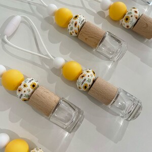 May include: A set of five car air fresheners with a white string for hanging. Each air freshener has a clear glass bottle with a wooden top, a white bead, a yellow bead, and a white bead with a sunflower pattern.