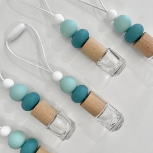May include: Five car air fresheners with a white string for hanging. Each air freshener has a clear glass bottle with a wooden top and three silicone beads in shades of blue and white.