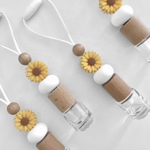 May include: Four car air fresheners with a white string, wooden beads, white silicone beads, and a yellow sunflower charm. The air fresheners are filled with clear liquid.