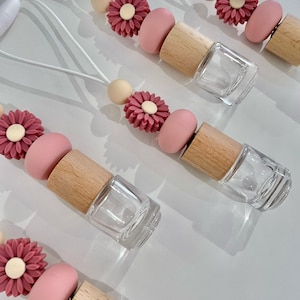 May include: Five pink and beige car air fresheners with a floral design. Each air freshener has a small glass bottle with a wooden cap and a string for hanging.