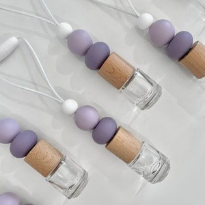 May include: Five car air fresheners with a white string for hanging. Each air freshener has a wooden cap and a clear glass bottle. The beads are purple, lavender, and white.