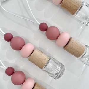 May include: Four car air fresheners with pink and red silicone beads and wooden caps. The air fresheners are attached to white strings.