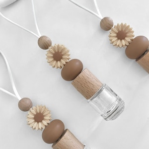 May include: Three car air fresheners with a brown and beige sunflower design. Each air freshener has a wooden cap and a clear glass bottle.