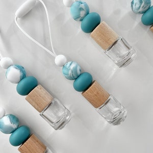 May include: A collection of small glass bottles with wooden tops and white cords. Each bottle is decorated with a string of beads in white, teal, and marbled blue. These bottles are likely for essential oils or perfumes.