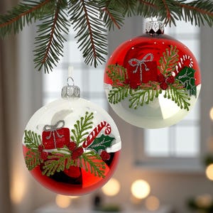 May include: Two Christmas ornaments with red and white sections, decorated with gift boxes, candy canes, and greenery. The ornaments are hanging from a pine branch, creating a festive holiday scene. The ornaments have silver tops.