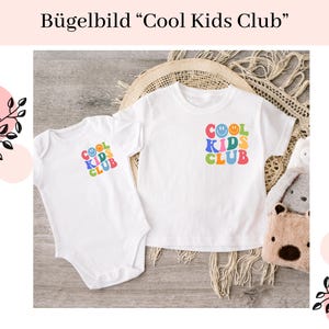 Könnte beinhalten: Zwei weiße T-Shirts mit dem Text "Cool Kids Club" in bunten Buchstaben und Smileys. Die Shirts liegen auf einer hellbraunen Oberfläche mit einer gewebten Textur.