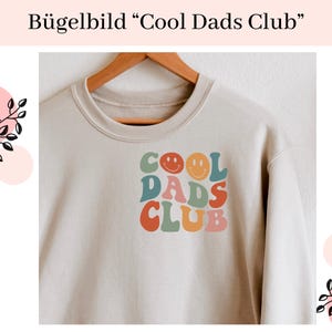 Könnte beinhalten: Ein beiger Pullover mit dem Text "Cool Dads Club" in bunten Retro-Lettern und Smileys.