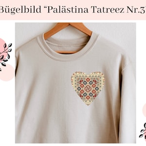 Könnte beinhalten: Ein beiger Pullover mit einem herzförmigen Bügelbild. Das Bügelbild zeigt ein farbenfrohes geometrisches Design mit roten, blauen und gelben Akzenten. Der Text "Palästina Tatreez Nr.3" ist über dem Pullover gedruckt.