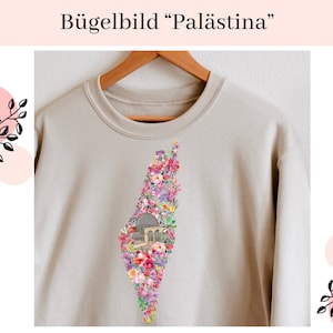 Könnte beinhalten: Beiges Sweatshirt mit floralem Design in Form einer Landkarte und einer Gebäudeillustration. Der Text "Bügelbild 'Palästina'" steht oben. Das florale Design besteht aus rosa, lila und grünen Blumen.