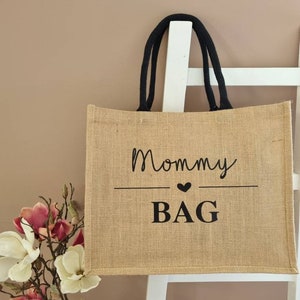 May include: A brown burlap tote bag with black handles and the text "Mommy Bag" printed on the front in black.