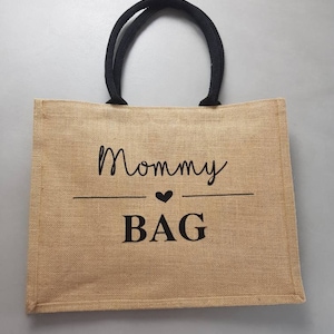 May include: A brown jute tote bag with black handles and the text "Mommy Bag" printed in black with a small heart symbol.