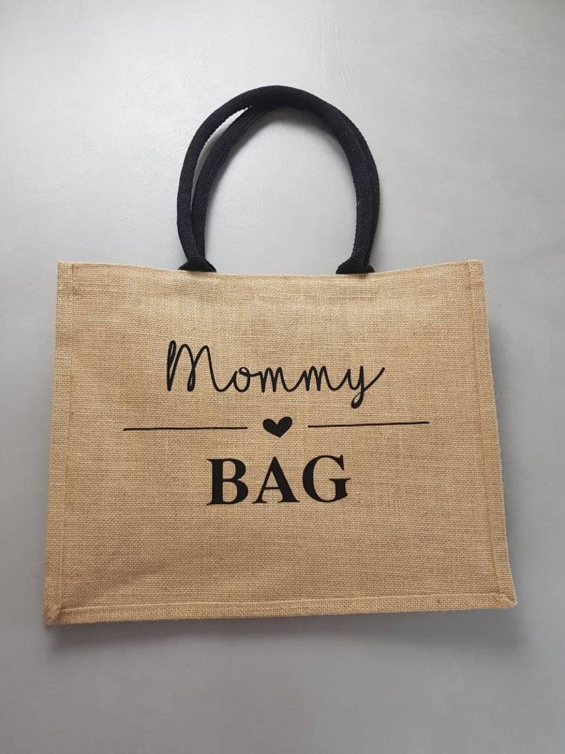May include: A brown jute tote bag with black handles and the text "Mommy Bag" printed in black with a small heart symbol.