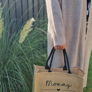 May include: A brown burlap tote bag with black handles and the text "Mommy Bag" with a heart symbol.