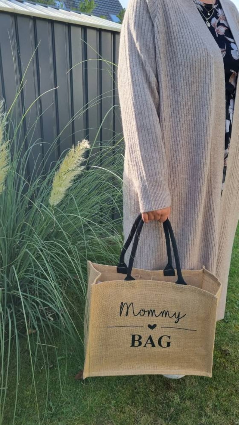 May include: A brown burlap tote bag with black handles and the text "Mommy Bag" with a heart symbol.