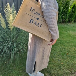 May include: A brown burlap tote bag with black text that reads "Mommy Bag" with a small heart symbol.