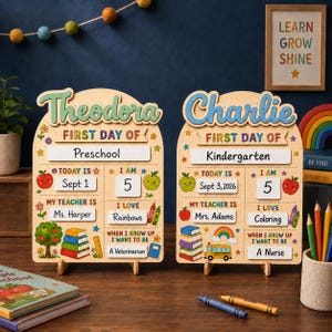 May include: Two arched wooden signs for the first day of school, personalised with the names Theodora and Charlie. Each sign features sections for grade, date, age, teacher, interests, and future goals, decorated with colourful illustrations of apples, books, and rainbows.