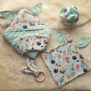 Könnte beinhalten: Ein Set Babyartikel mit Waldmotiv. Das Set beinhaltet ein Kapuzenhandtuch, ein Spucktuch, einen Beißring und eine Rassel. Die Artikel sind alle aus weichem, saugfähigem Stoff gefertigt und mit niedlichen Tiermotiven verziert.