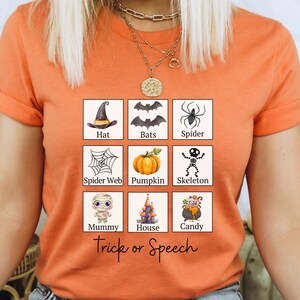 May include: Orange t-shirt with a Halloween-themed graphic. The graphic features nine illustrated squares with Halloween icons like a witch's hat, bats, spider, spider web, pumpkin, skeleton, mummy, haunted house, and candy. The text "Trick or Speech" is below the squares.