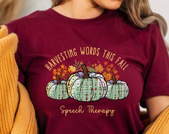 May include: Burgundy t-shirt with a fall-themed graphic. The design features three pumpkins with speech therapy symbols, surrounded by autumn leaves, and the text "Harvesting Words This Fall Speech Therapy."