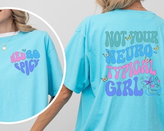 May include: A light blue t-shirt featuring the text "Not Your Neuro-Typical Girl" in a colourful, retro font. The text is surrounded by butterflies and a stylised face.