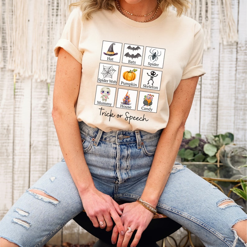 May include: Cream-colored t-shirt featuring a grid of Halloween-themed illustrations: a witch's hat, bats, a spider, a spider web, a pumpkin, a skeleton, a mummy, a haunted house, and a cauldron of candy. The text "Trick or Speech" is below the grid.