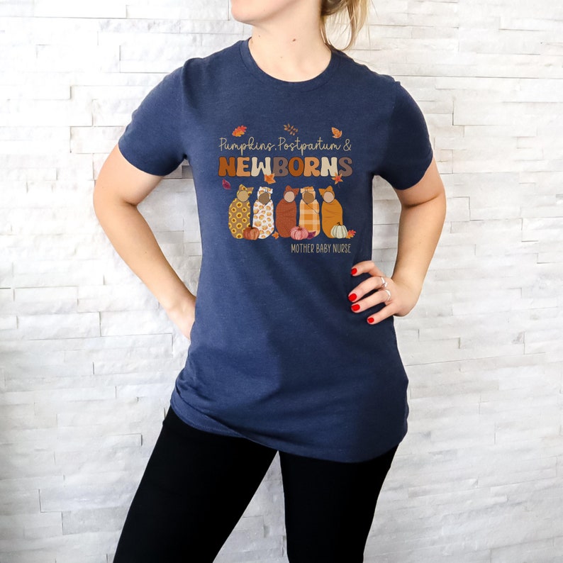 May include: A navy blue t-shirt featuring the text "Pumpkins, Postpartum & Newborns" and an illustration of swaddled babies and pumpkins. The shirt also includes the text "Mother Baby Nurse".