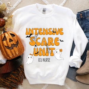 May include: White sweatshirt featuring the words "Intensive Scare Unit" in orange, with bat, spiderweb, and ghost graphics. The text "ICU Nurse" is below the main text. A decorative pumpkin and autumn leaves are in the background.