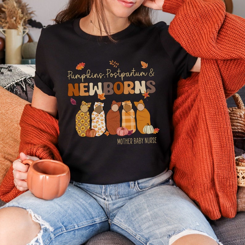 May include: Black t-shirt with the text "Pumpkins, Postpartum & NEWBORNS" in brown and orange lettering. The shirt features illustrations of swaddled babies, pumpkins, and autumn leaves. The words "MOTHER BABY NURSE" are printed below the illustrations.