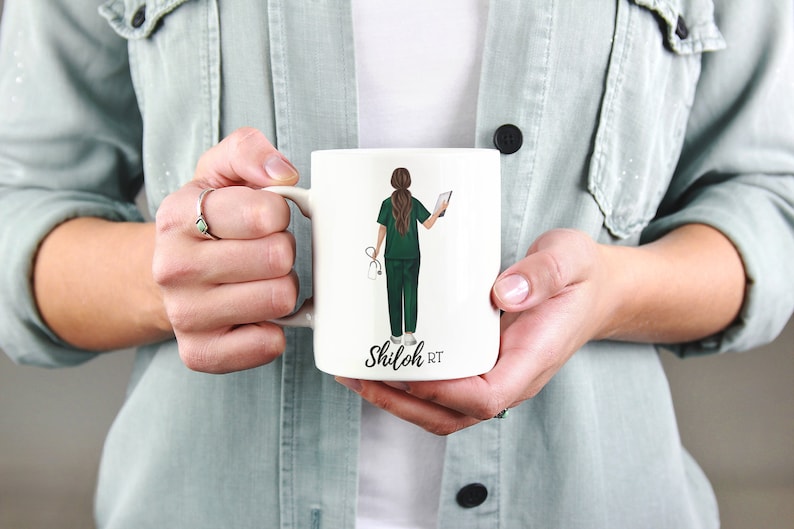 Puede incluir: Taza de cer&aacute;mica blanca con una ilustraci&oacute;n verde y marr&oacute;n de una persona con bata m&eacute;dica sosteniendo un estetoscopio y una tableta. El texto "Shiloh RT" est&aacute; impreso en la taza.