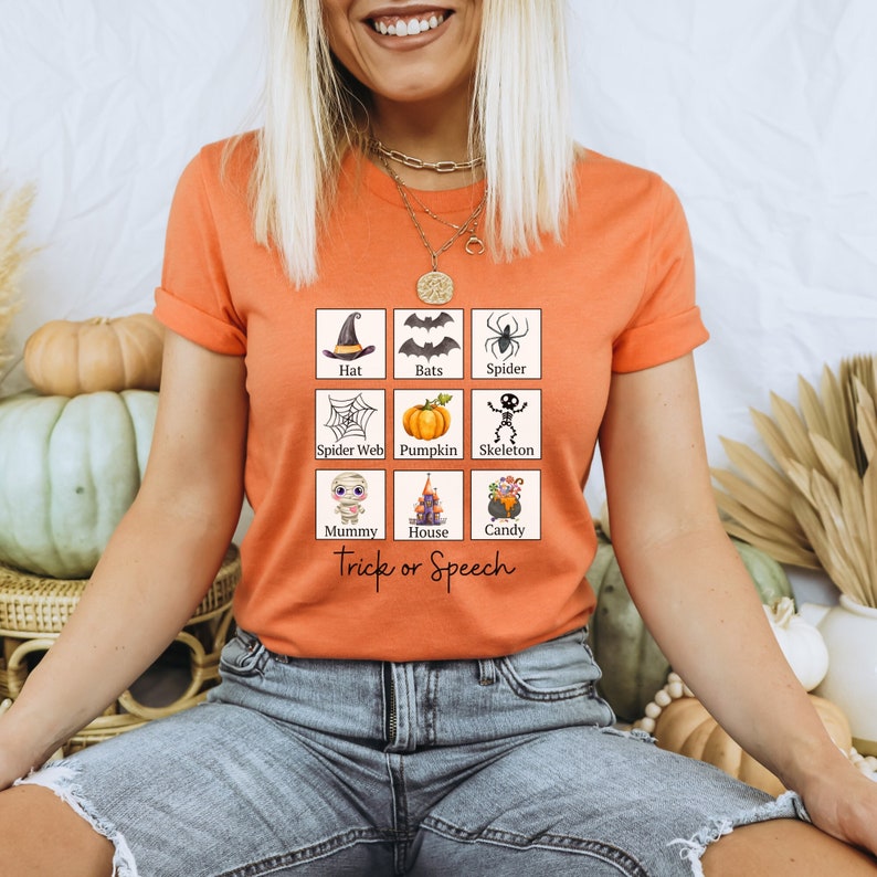 May include: Orange t-shirt with a Halloween-themed graphic. The graphic features nine illustrated squares with Halloween icons like a witch's hat, bats, spider, spider web, pumpkin, skeleton, mummy, haunted house, and candy. The text "Trick or Speech" is below the squares.