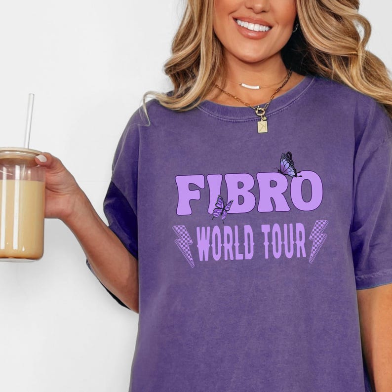 May include: Purple t-shirt with the text "FIBRO WORLD TOUR" in a light purple color with two butterfly graphics.