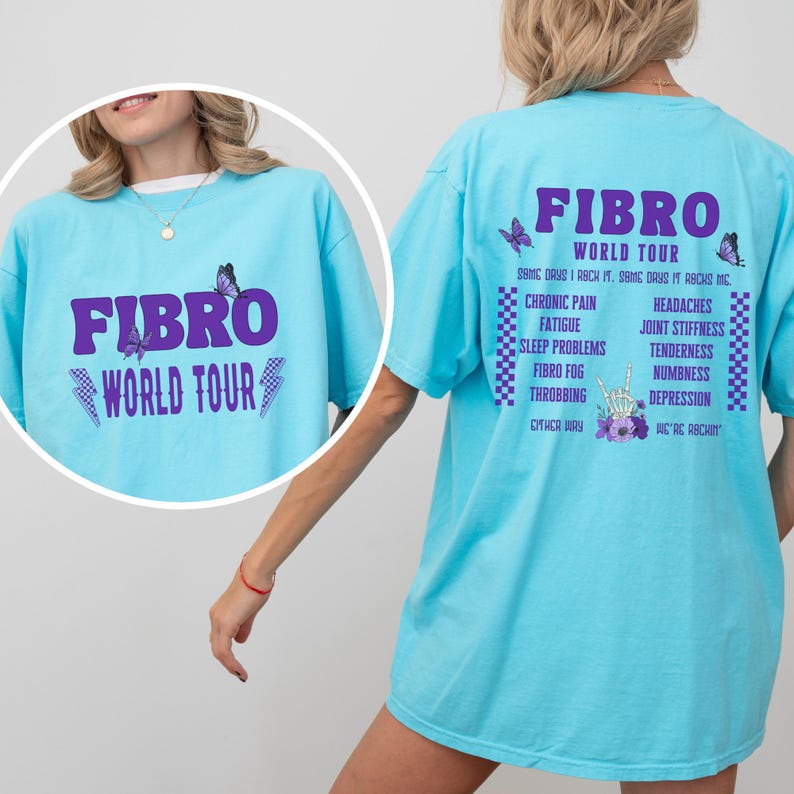 May include: A light blue t-shirt with the text "FIBRO WORLD TOUR" in purple on the front and a list of symptoms associated with fibromyalgia on the back. The back also includes a butterfly graphic and a hand with a peace sign.