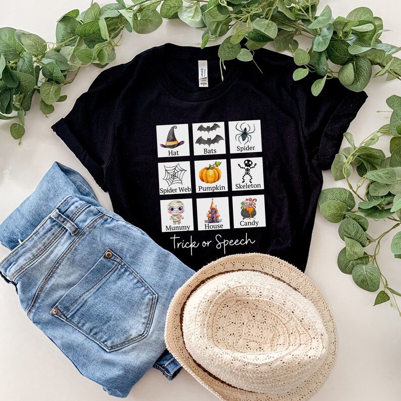 May include: Black t-shirt with a Halloween-themed graphic featuring a witch's hat, bats, spider, spider web, pumpkin, skeleton, mummy, haunted house, and candy. The text "Trick or Speech" is below the graphic. The shirt is paired with blue jeans and a straw hat.