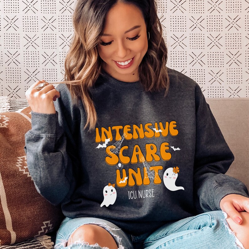 May include: Dark grey sweatshirt featuring the words "INTENSIVE SCARE UNIT" in orange and white, with bat, spiderweb, and ghost graphics. The text "ICU NURSE" is below. The design is a Halloween theme.