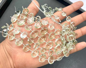 Puede incluir: Hebras de cuentas de piedras preciosas facetadas de color verde claro. Las cuentas son ovaladas y redondas, ensartadas en un alambre fino y transparente. Las piedras preciosas tienen una calidad translúcida y se muestran en una mano abierta.