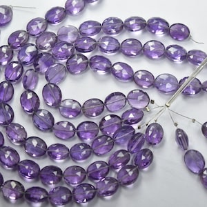 Può includere: Una collana di perle di ametista viola, di forma ovale e sfaccettate, infilate su un filo.