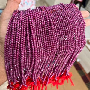 May include: A strand of ruby beads, each bead is faceted and has a deep pink colour. The beads are strung on a thin thread and are tied together at the ends with red string.