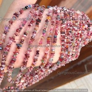 Könnte beinhalten: Stränge bunter Edelsteinperlen in Rosa, Rot, Lila und Blau. Die Perlen sind kleine, unregelmäßige Chips, die zu einem strukturierten Aussehen aufgereiht sind. Das Bild zeigt mehrere Stränge, was auf ein Schmuckthema hindeutet.