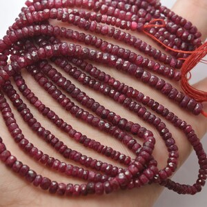 May include: A strand of ruby beads, with a faceted, slightly irregular shape. The beads are a deep red color and are strung on a thin thread. The beads are arranged in a loose, flowing pattern.