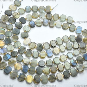 May include: A strand of faceted labradorite gemstone beads in shades of gray, blue, and gold. The beads are octagonal in shape and have a smooth, polished finish.