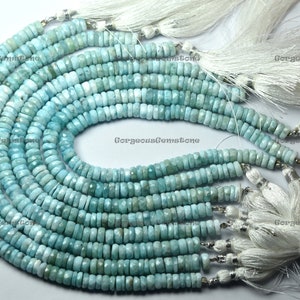 Könnte beinhalten: Eine Strähne aus 10 hellblauen Edelsteinperlen mit weißen Quasten. Die Perlen sind facettiert und haben eine leicht unregelmäßige Form. Die Strähne ist etwa 45 cm lang.