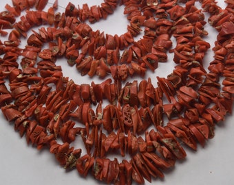 May include: A strand of red coral beads, each bead is a unique, irregular shape and has a rough, textured surface.