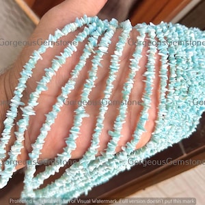 Könnte beinhalten: Eine Hand hält mehrere Stränge hellblauer Edelstein-Chip-Perlen. Die Perlen sind eine Mischung aus Hellblau und Weiß, mit unregelmäßiger Form. Das Bild hat den Text "Gorgeous Gemstone" an mehreren Stellen.