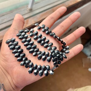 May include: A strand of black faceted gemstone beads. The beads are strung on a thin wire and are arranged in a loose, flowing pattern.