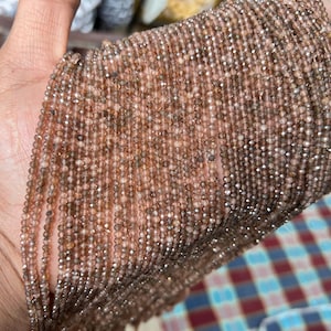 May include: A strand of brown faceted gemstone beads. The beads are small and round, and they are strung on a clear thread. The beads are arranged in a loose, flowing pattern.
